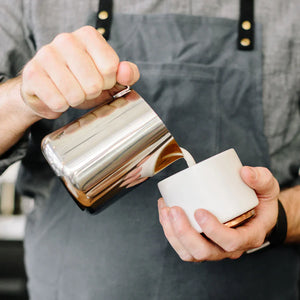 Barista hælder mælk fra en poleret kande i rustfrit stål, del af Espresso tilbehør og mælkekande, alt om kaffe.